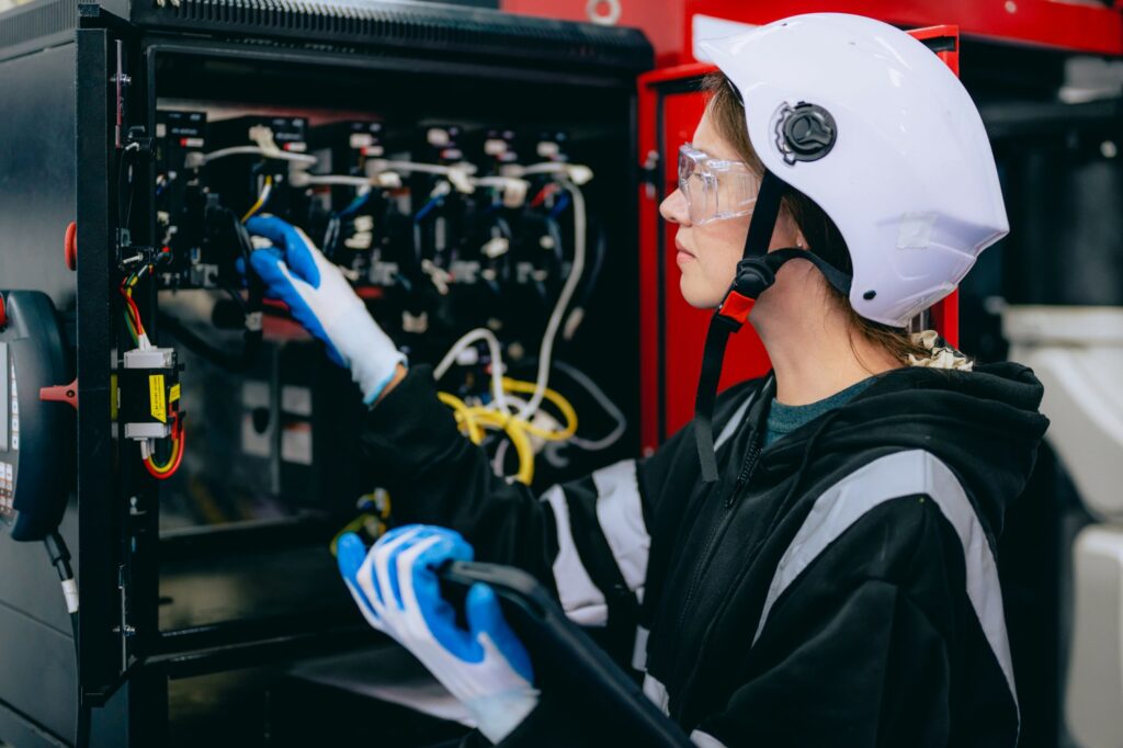 Apprentie électricienne casquée intervenant sur le câblage d'une armoire électrique