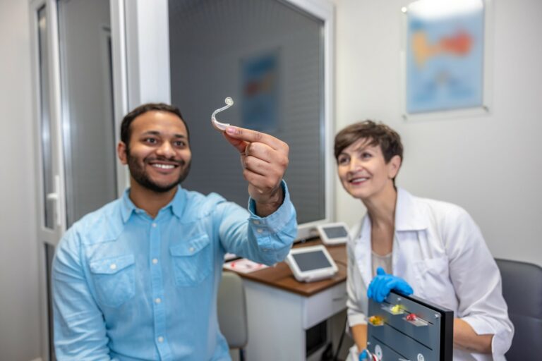 Patient souriant tenant un appareil auditif contour d'oreille, aux côtés de son audioprothésiste