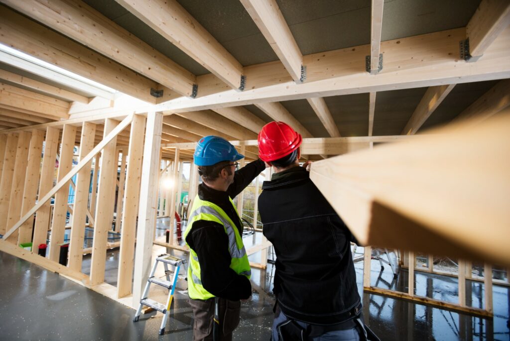 Deux charpentiers casqués vérifiant une poutre sur un chantier d'ossature bois
